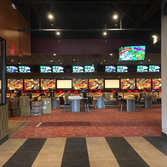 A bowling alley with vibrant walls, seating, and scattered boxes—perfect for a commercial flooring company’s new flooring installation project.