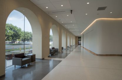 A modern hallway with large arched windows, armchairs, and polished floors by a top flooring installation company, trees visible outside.