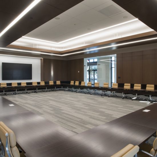 A large conference room with U-shaped tables, beige chairs, wood paneling, and floors by a professional flooring installation company.