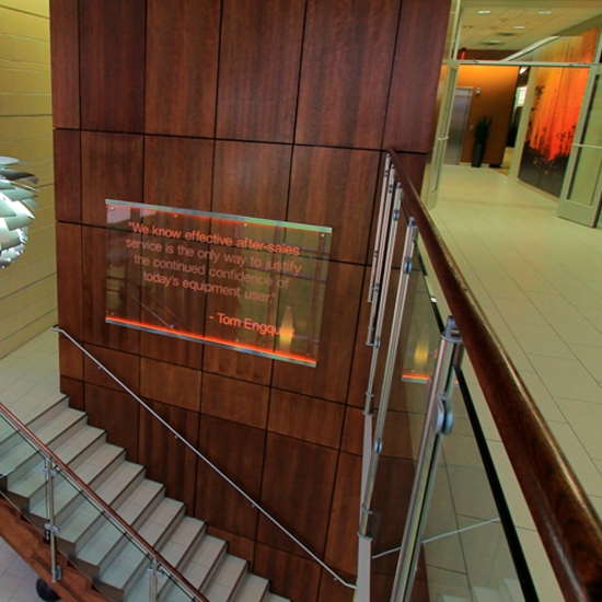 Wood-paneled wall with an illuminated quote sign near a staircase, showcasing work by a leading commercial flooring company in a modern office building.