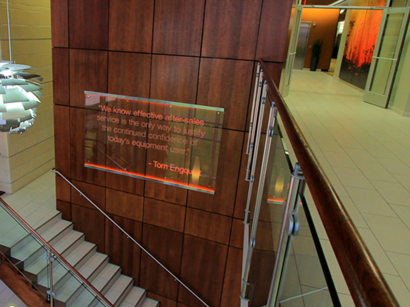 Wood-paneled wall with an illuminated quote sign near a staircase, showcasing work by a leading commercial flooring company in a modern office building.