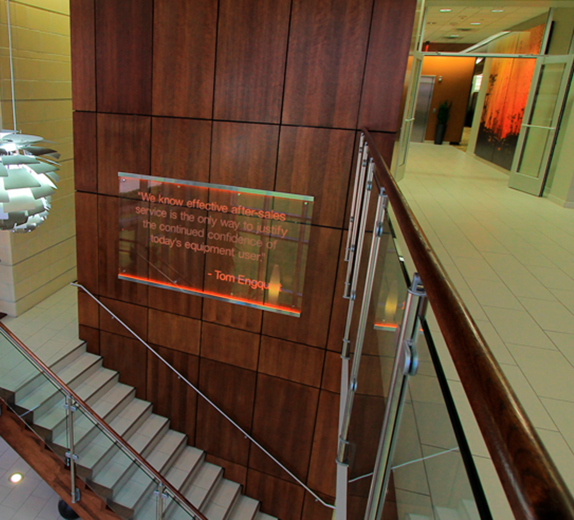 Wood-paneled wall with an illuminated quote sign near a staircase, showcasing work by a leading commercial flooring company in a modern office building.