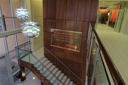 Modern indoor staircase with glass railings and wood panel wall highlights expert new flooring installation in a brightly-lit office building.