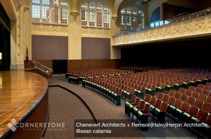 Large, empty auditorium with rows of red and green seats, a wooden stage—showcasing work by a top flooring installation company.