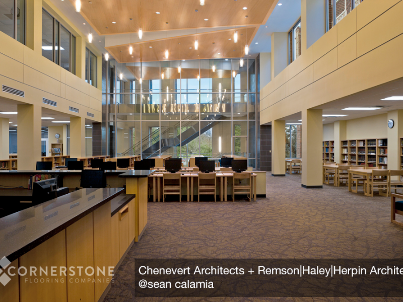 Spacious modern library interior with new flooring installation, high ceilings, large windows, bookshelves, and rows of computers on desks.