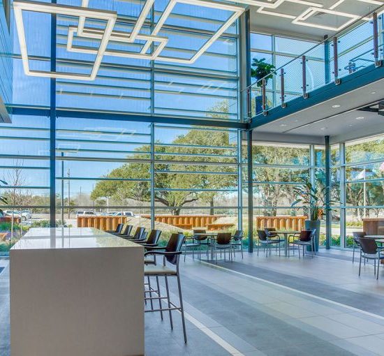 Modern office lobby with new flooring installation, large windows, seating area, and geometric ceiling lights, featuring outdoor views.
