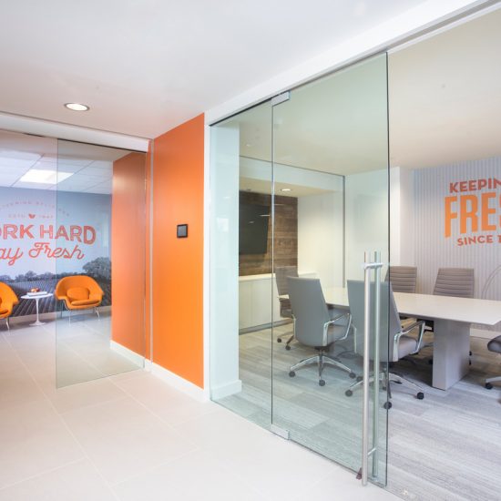 Modern office space with glass walls, orange accents, and flooring by a top flooring installation company.