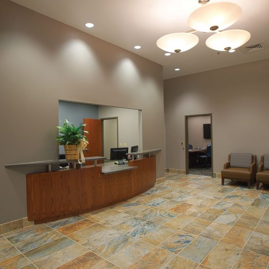 Reception area with a wooden desk, awards, chairs, and tiled floor by a flooring contractor in a modern office setting.