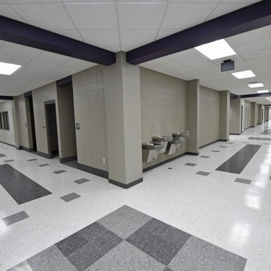 Empty school hallway with tiled floors by a flooring installation company, beige walls, water fountains, and fluorescent ceiling lights.
