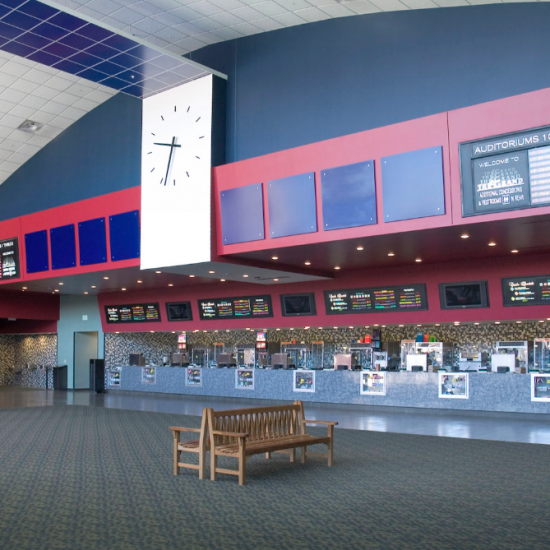 Movie theater lobby with a large clock, sleek flooring by a leading commercial flooring company, and digital menu boards above the counter.