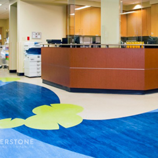 Reception area in a medical facility with a wood-paneled desk and stylish flooring by a commercial flooring company, plus office equipment in the background.