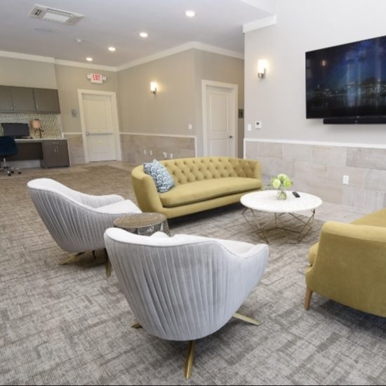 A modern lounge with a yellow sofa, gray armchairs, sleek flooring by a commercial flooring company, and a wall-mounted TV.