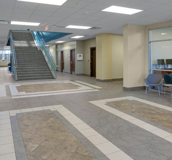 A modern building lobby with new flooring installation, blue benches, glass-walled rooms, and a staircase leading to an upper floor.
