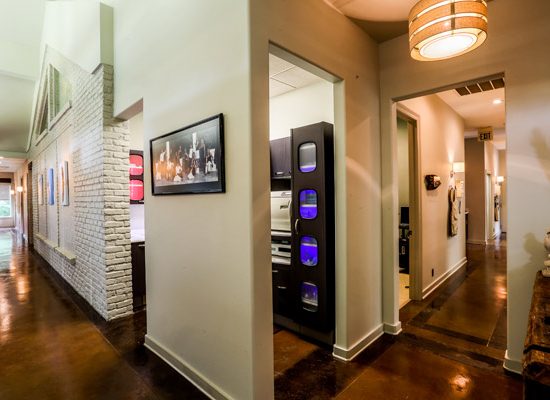 Modern office hallway with polished floors by a commercial flooring company, white walls, framed art, and a purple-lit kitchenette.