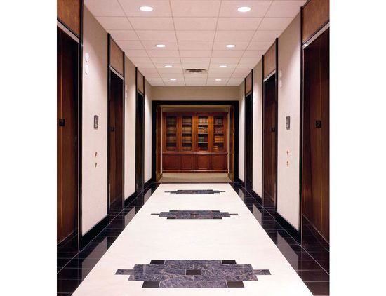 A hallway with multiple elevator doors, new flooring installation, and a wooden cabinet at the end of the corridor.