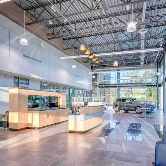 A modern car dealership showroom with sleek flooring installed by a professional flooring contractor, plus a reception desk and glass walls.