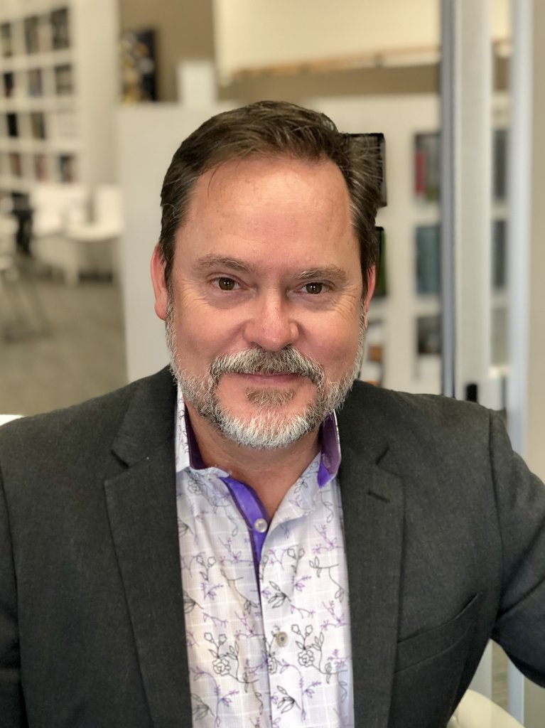A man with short brown hair and a beard sits indoors, possibly in a modern office after new flooring installation by a commercial flooring company.